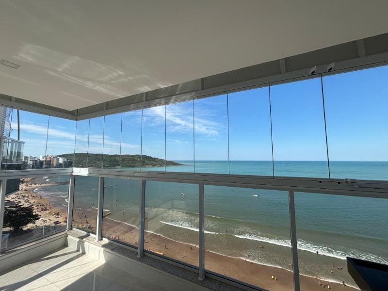 Varanda envidraçada de um apartamento na Praia do Morro, com vista para a praia, o mar e uma ilha ao fundo